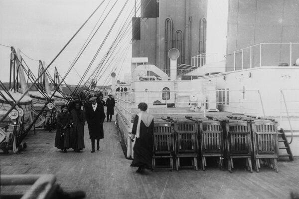 Passengers stroll past neatly arranged and folded deck chairs on the deck of the Titanic.