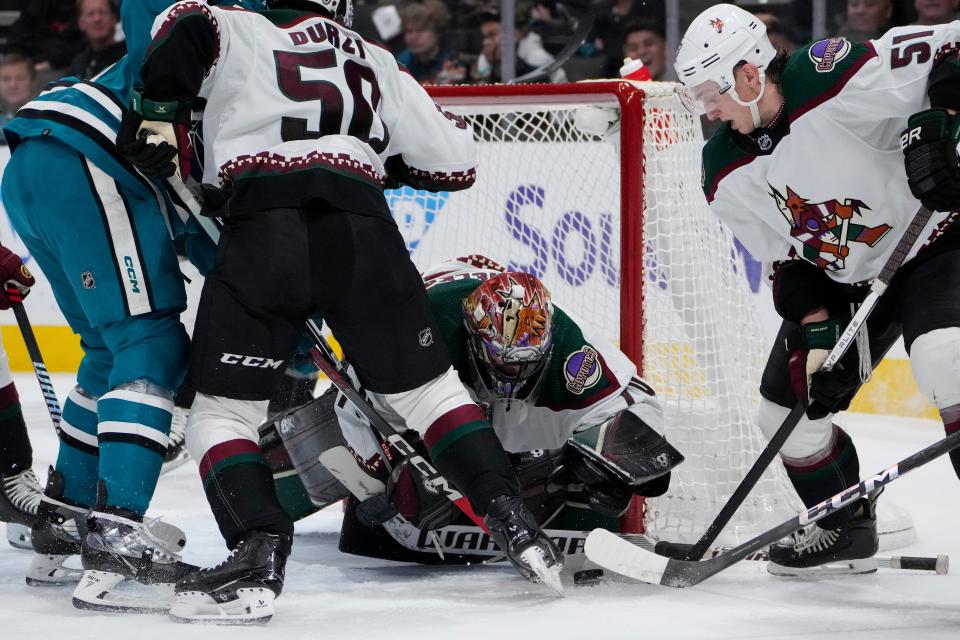 Arizona Coyotes goaltender Karel Vejmelka, center, covers the puck during the first period of the team's NHL hockey game against the San Jose Sharks on Thursday, Dec. 21, 2023, in San Jose, Calif. (AP Photo/Godofredo A. Vásquez)