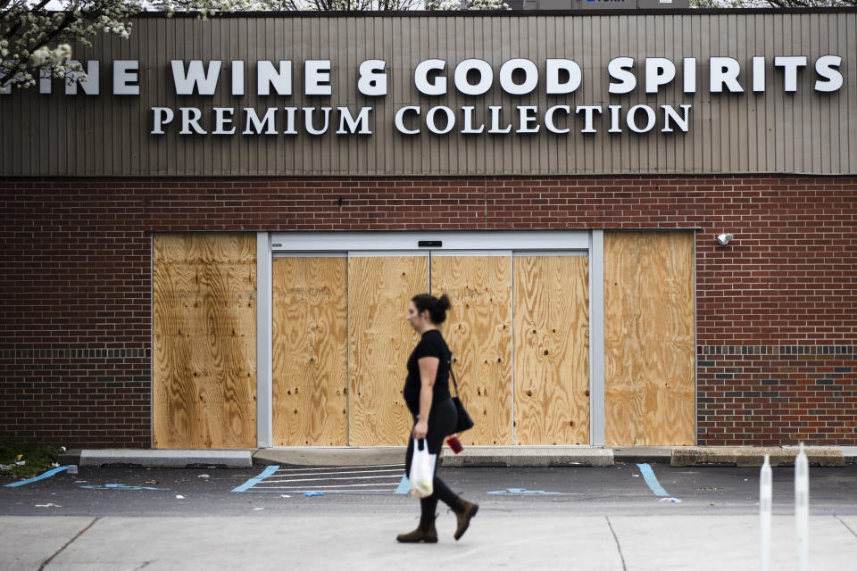 A pedestrian walks past a boarded up Wine and Spirits store in Philadelphia, Friday, March 20, 2020. Pennsylvania Gov. Tom Wolf directed all "non-life-sustaining" businesses to close their physical locations late Thursday and said state government would begin to enforce the edict starting early Saturday. (AP Photo/Matt Rourke)