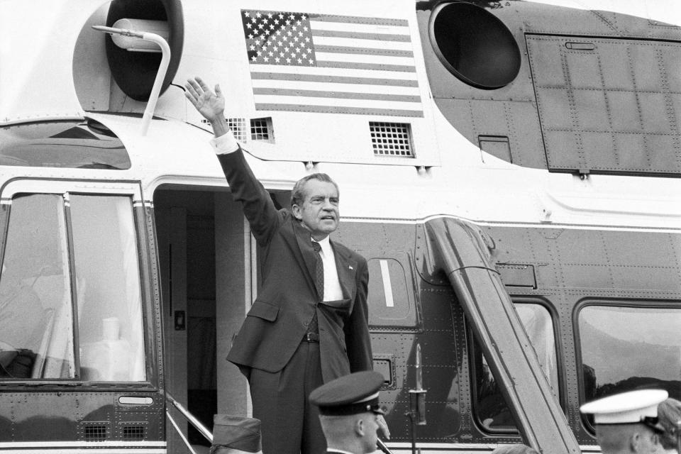 A black and white photo of Richard Nixon waving in front of a helicopter.