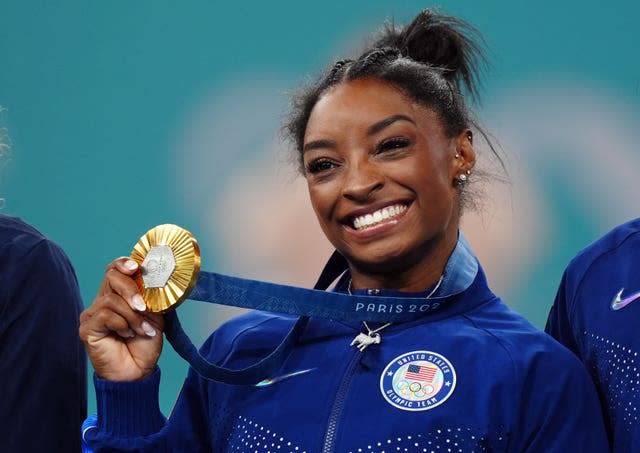 A smiling Simone Biles holds up one of her gold medals.