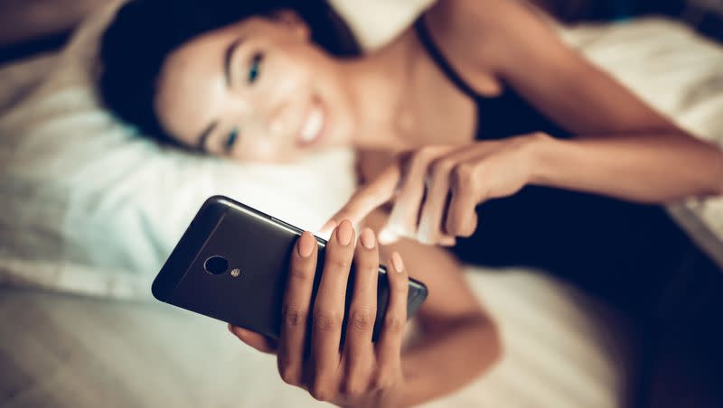 A woman uses a smartphone while lying in bed. 