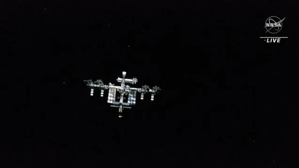 The international space station as seen from SpaceX's crew dragon as a silver spacecraft in the black of space.