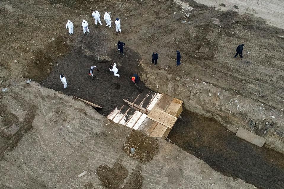 Workers wearing personal protective equipment bury bodies in a trench on Hart Island, Thursday, April 9, 2020, in the Bronx borough of New York. On Thursday, New York City’s medical examiner confirmed that the city has shortened the amount of time it will hold on to remains to 14 days from 30 days before they will be transferred for temporary internment at a City Cemetery. Earlier in the week, Mayor Bill DeBlasio said that officials have explored the possibility of temporary burials on Hart Island, a strip of land in Long Island Sound that has long served as the city’s potter’s field.  (AP Photo/John Minchillo) ORG XMIT: NYJM114