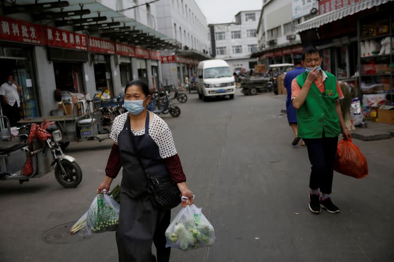 People wearing face masks carry bags of vegetables inside the Yuegezhuang wholesale market, following new cases of coronavirus disease (COVID-19) infections in Beijing