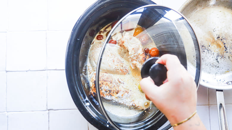 hand putting lid on slow cooker with chicken