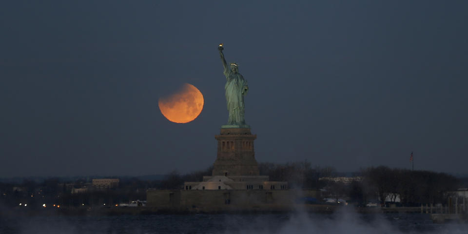 NEW YORK, NY - JANUARY 31: The eclipsed super blue blood moon sets next to the Statue of Liberty at sunrise on January 30, 2018 in New York City. (Photo by Gary Hershorn/Corbis via Getty Images)