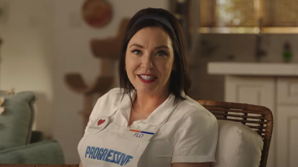 Stephanie Courtney smiles as she sits on the couch explaining insurance in Progressive.