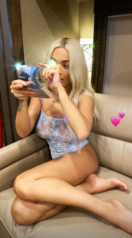 A photo of Rita Ora posing on a couch wearing a blue sheer lace bodysuit.