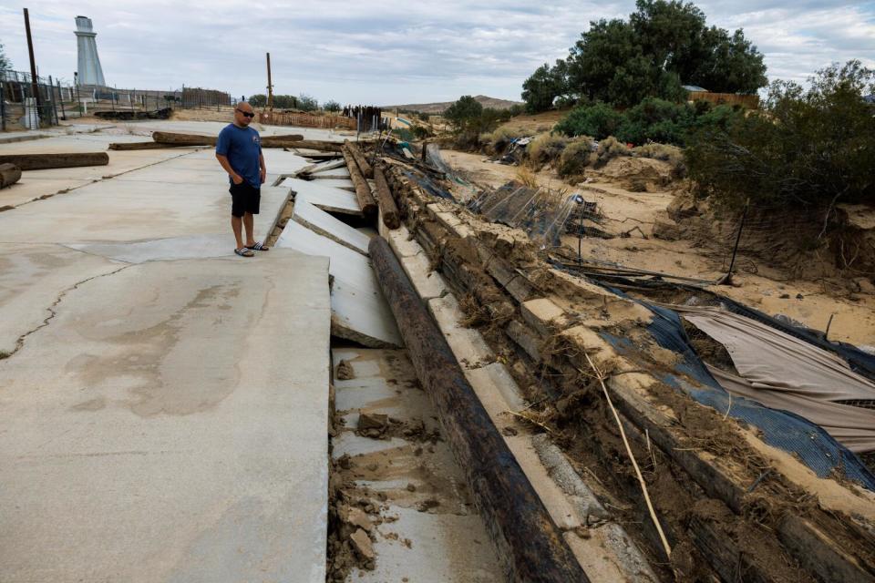 A man looks at buckled pavement and other storm damage