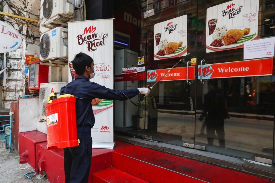 A member of Yangon City and Development Committee sprays disinfectant on a restaurant's front doors to help curb the spread of the coronavirus, Sunday, March 29, 2020.