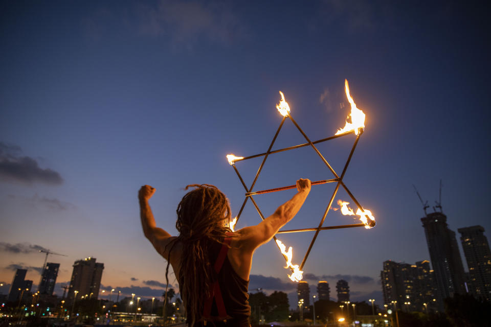 An Israeli juggler holds a model in the shape of the Star of David on a bridge during a protest against Israel's Prime Minister Benjamin Netanyahu in Tel Aviv, Israel, Saturday, Aug. 22, 2020. (AP Photo/Oded Balilty)