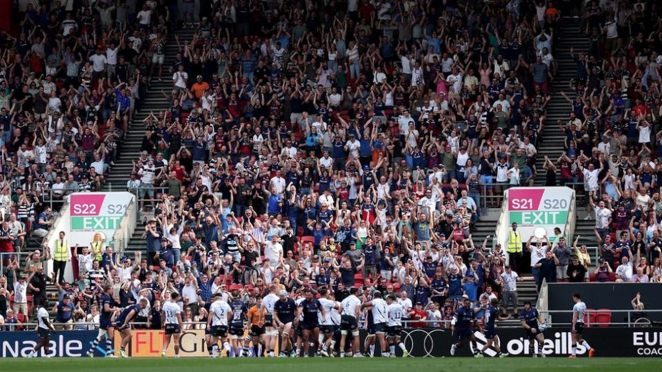 Bristol Bears players celebrate a try against Saracens with fans celebrating in the stands behind them