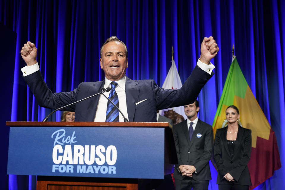 Los Angeles mayoral candidate Rick Caruso, both fists in the air, at the microphone, with his family behind him on stage.