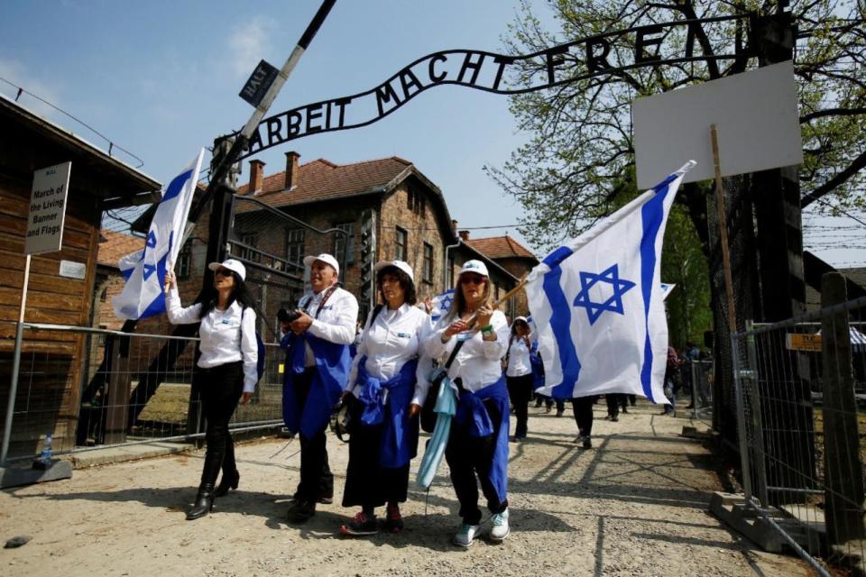 People wave Israeli flags in front of a gate with the words “Arbeit macht frei” (Work sets you free) in the former Nazi death camp of Auschwitz as thousands of people, mostly youth from all over the world gathered for the annual “March of the Living” to commemorate the Holocaust  in Oswiecim, Poland May 5, 2016. (Kacper Pempel/REUTERS)