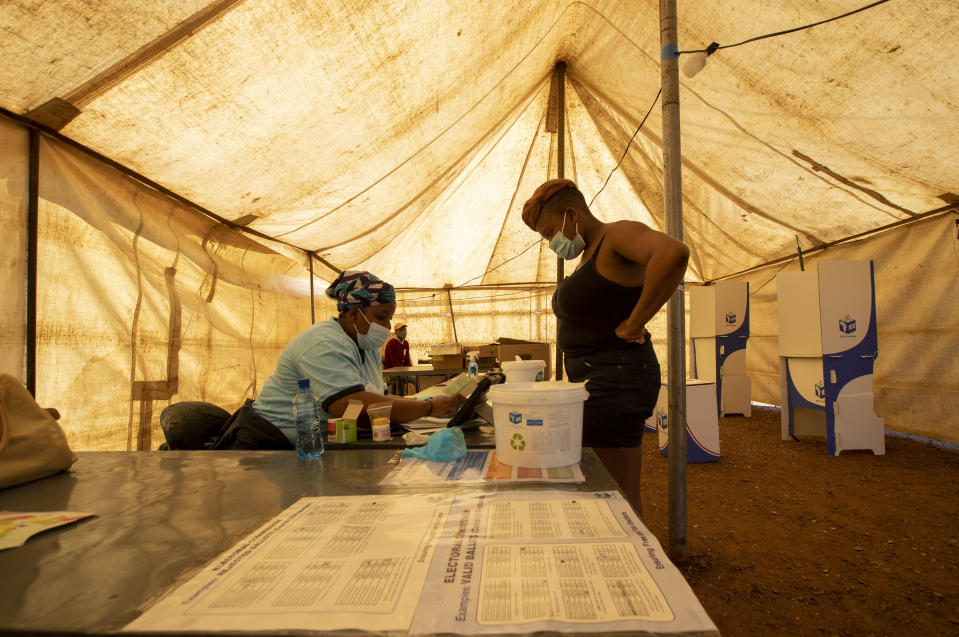 A woman stands as her identity is checked by electoral commission official inside polling station in Thokoza, east of Johannesburg, South Africa, Monday, Nov. 1, 2021. South Africa is holding crucial local elections Monday, the country has been hit by a series of crippling power blackouts that many critics say highlight poor governance. (AP Photo/Themba Hadebe)