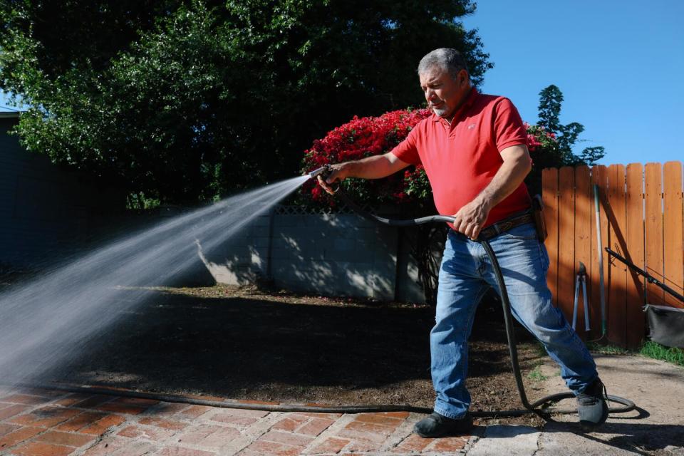 Joaquin Hurtado waters grass with a hose.