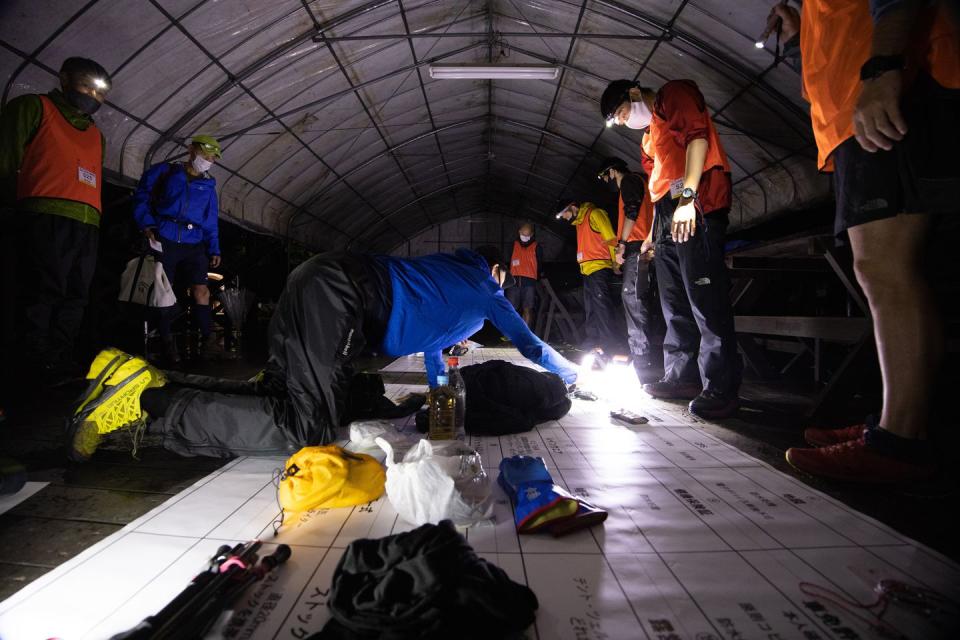 officials watch a runner lay out his mandatory 27 items before the trans japan selection event