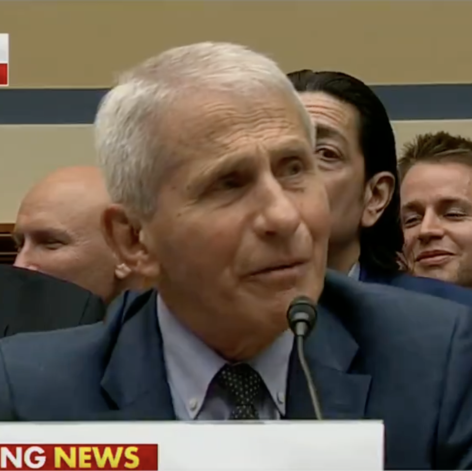 Dr. Anthony Fauci in a blue suit testifies at a Capitol Hill hearing. Several other people are seated behind him. The image is captioned 