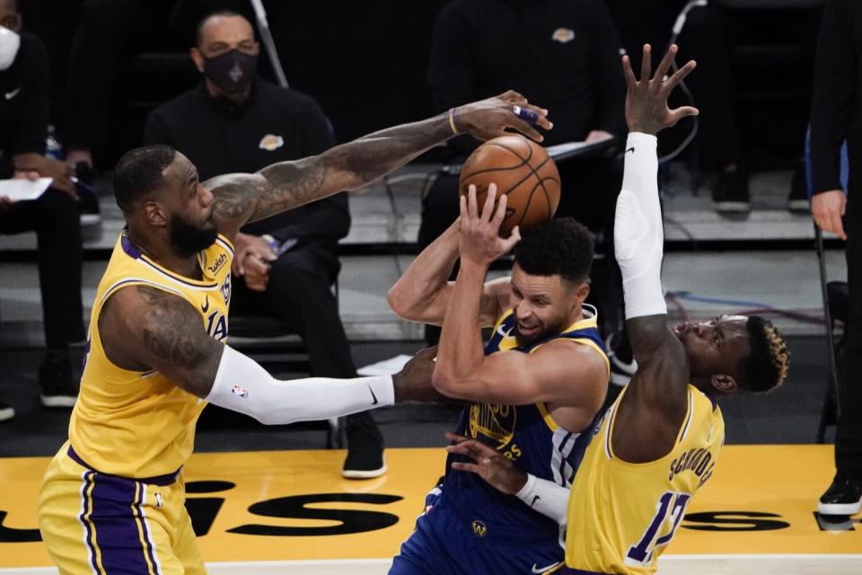 Lakers forward LeBron James, left, and guard Dennis Schroder, right, defend Warriors guard Stephen Curry as he drives.