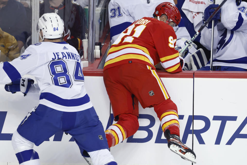 Calgary Flames center Nazem Kadri (91) is pushed into the Tampa Bay bench by Tampa Bay Lightning left wing Tanner Jeannot (84) during the first period of an NHL hockey game Saturday, Dec. 16, 2023, in Calgary, Alberta. (Larry MacDougal/The Canadian Press via AP)