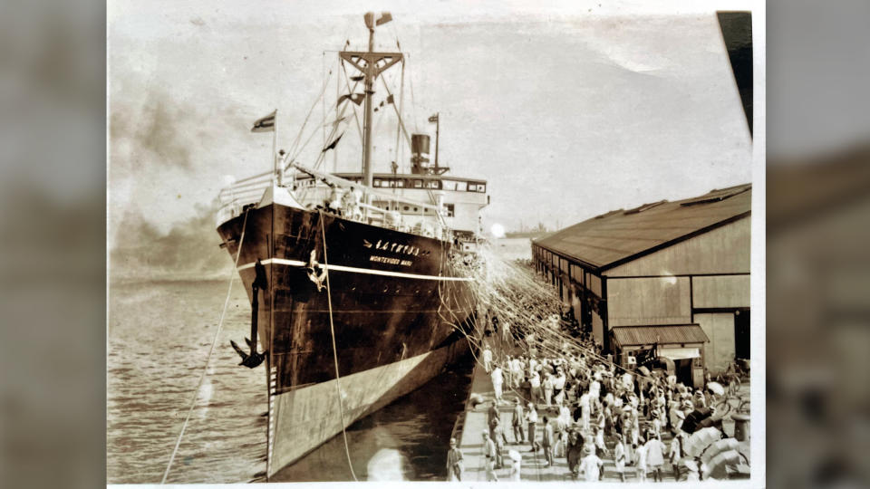 A black and white photo of the Montevideo Maru docking next to crowd of people on shore.