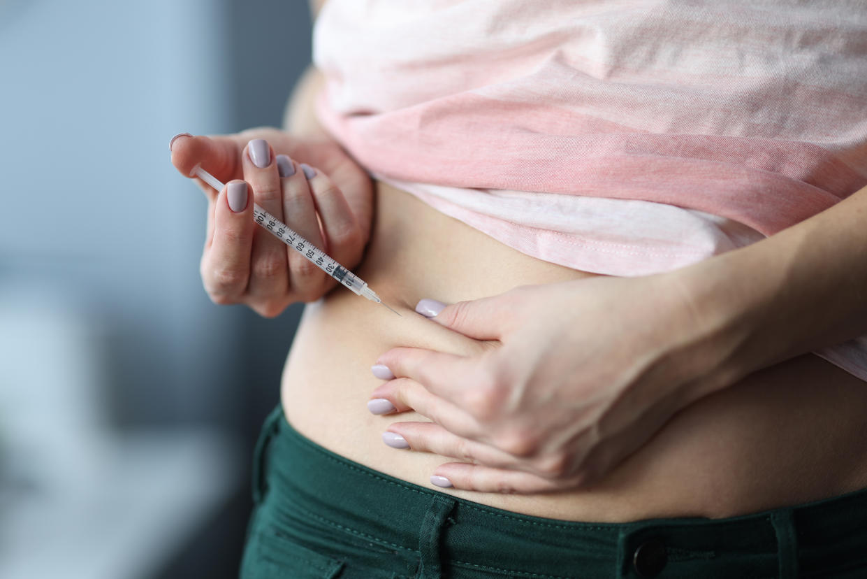 A woman injects a drug into her abdomen.