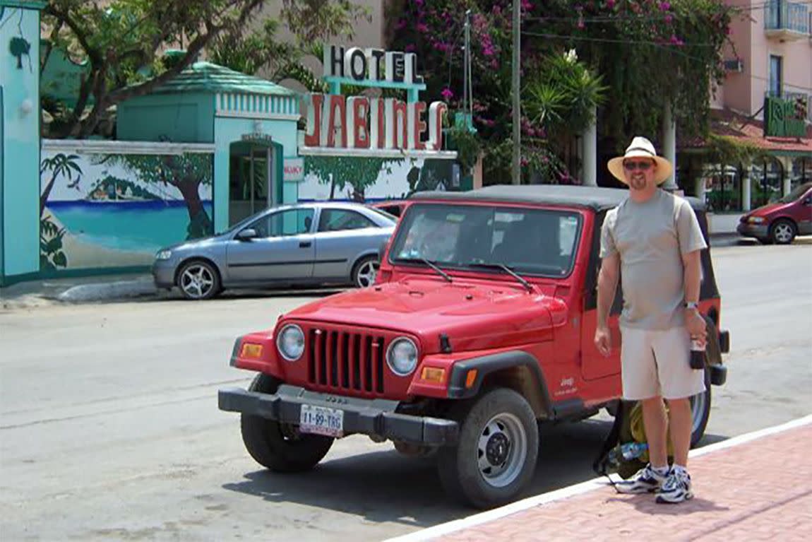 Man in hat posing with small red Jeep in front of Hotel Jabines.
