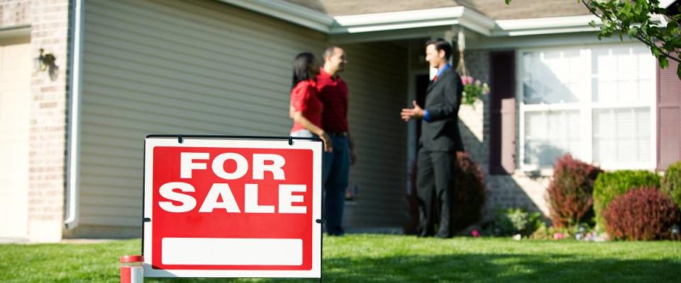 Couple talking with real estate agent outside house for sale.