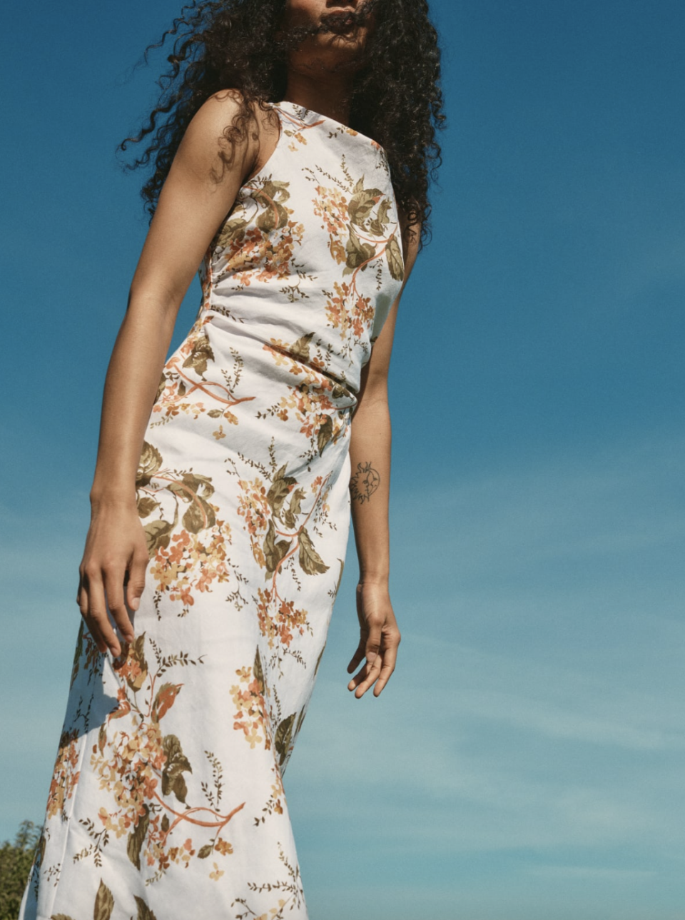 model with black afro against blue sky wearing white and floral Casette Linen Dress (photo via Reformation)