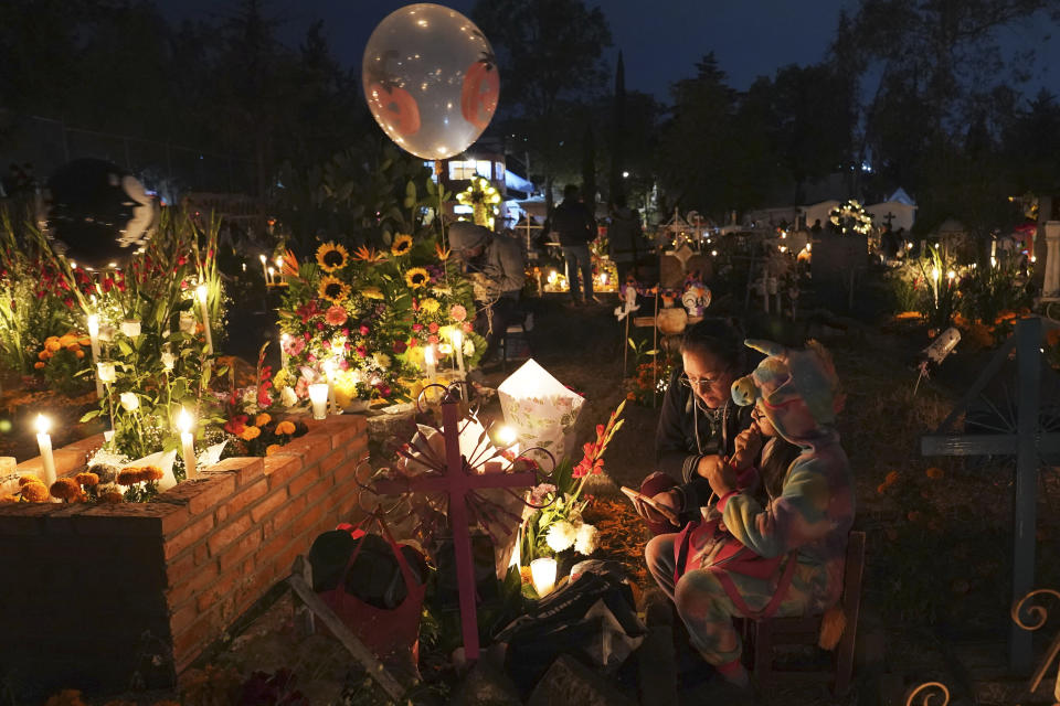 People sit around a child's tomb in the San Gregorio Atlapulco cemetery during Day of the Dead festivities on the outskirts of Mexico City, early Wednesday, Nov. 1, 2023. In a tradition that coincides with All Saints Day on Nov. 1 and All Souls Day on Nov. 2, families decorate graves with flowers and candles and spend the night in the cemetery, eating and drinking as they keep company with their dearly departed. (AP Photo/Marco Ugarte)