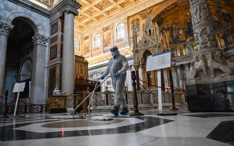 A man wearing protective overalls and mask cleans the floor of the churchyard of the Basilica of Saint Paul Outside The Walls (San Paolo Fuori Le Mura) in Rome, Churches are being disinfected in advance of reopening to worshipers - ANDREAS SOLARO/AFP via Getty Images