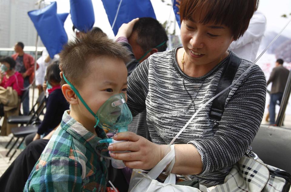 A woman helps her son put on a mask connected to a plastic bag with air taken in Laojun Mountain of Luanchuan county, during a promotional event on a hazy day in Zhengzhou, Henan province March 29, 2014. According to organizers, the event was held to promote fresh mountain air in the tourist resort and they hope to attract more visitors to the area, local media reported. China's plan for a market in air pollution permits promises to help clean up its air cheaply, but the move could prove just as useless as previous environmental policies unless the government stamps out lax enforcement and spotty data. Picture taken March 29, 2014. REUTERS/Stringer (CHINA - Tags: ENVIRONMENT SOCIETY POLITICS TRAVEL) CHINA OUT. NO COMMERCIAL OR EDITORIAL SALES IN CHINA