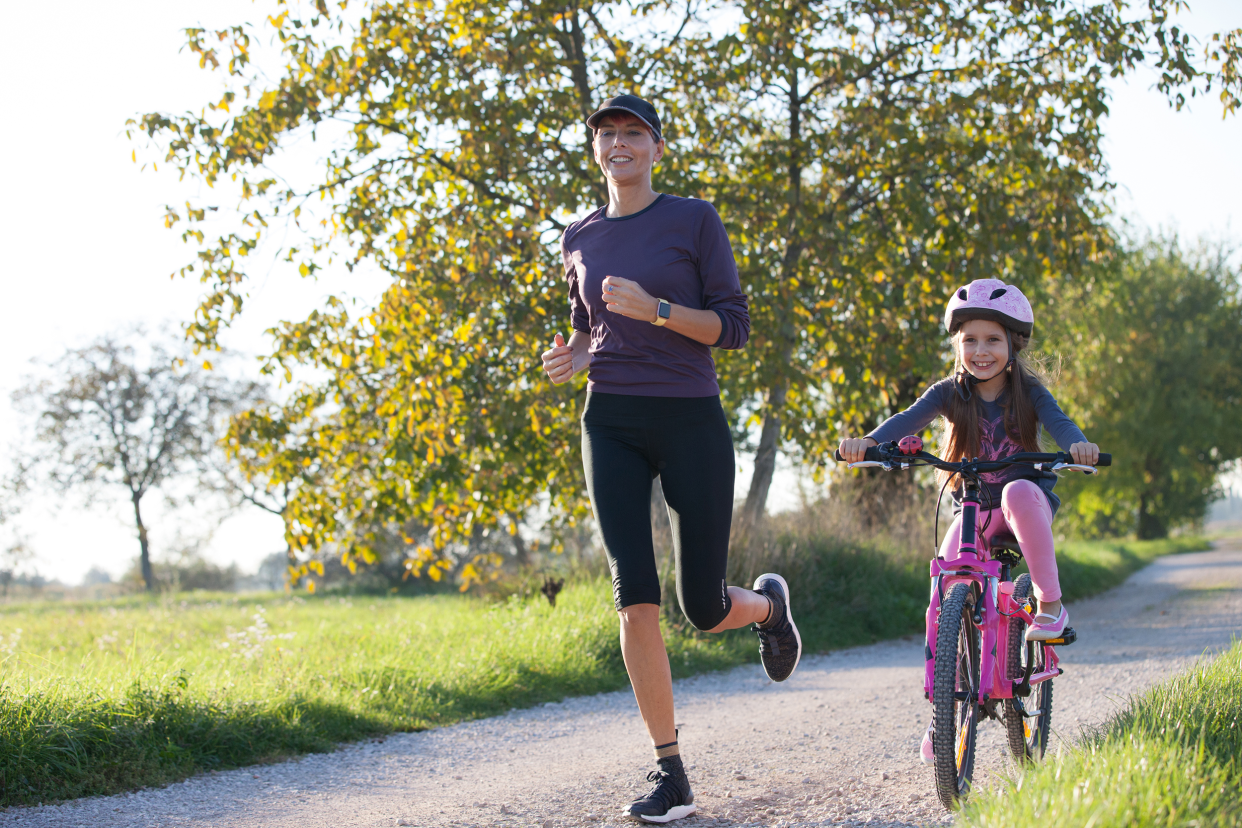 Mother jogging with her daughter biking behind her