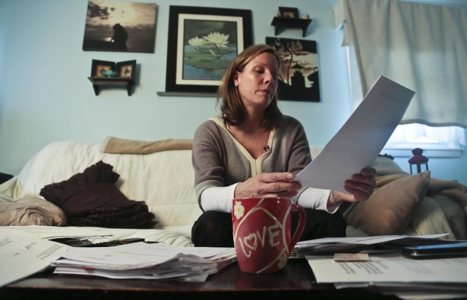 In this Tuesday, March 11, 2014 photo, Nora Milligan looks through a pile of legal healthcare documents before an interview at her home in Patchogue, N.Y. Milligan, a single mother, fought healthcare providers in court for denial of care to her heroin-addicted son. Having exhausted her finances for his care, she continues to live in the home she raised him even as it is being foreclosed. (AP Photo/Bebeto Matthews)