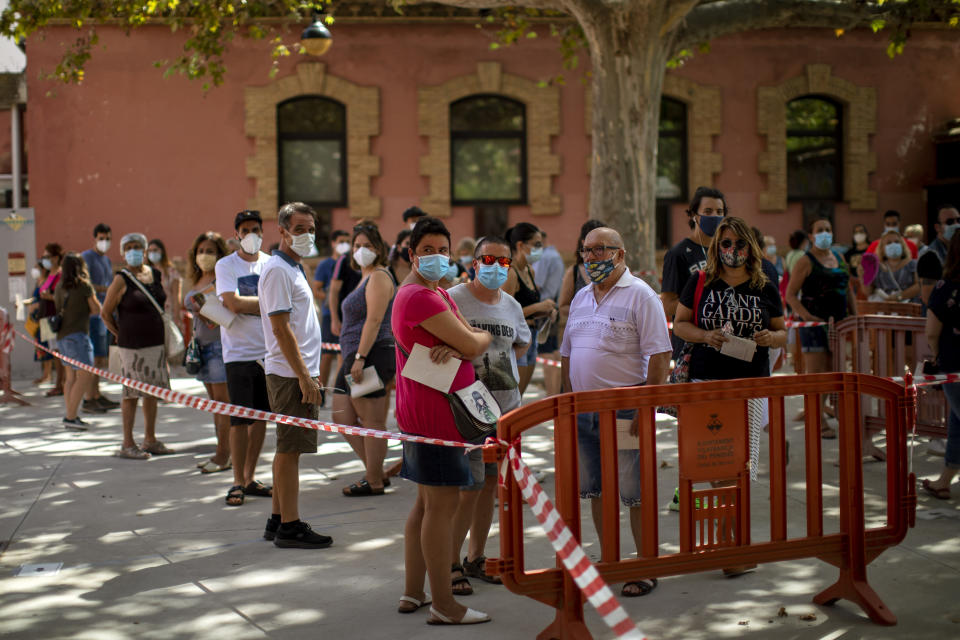 People wearing face masks queue up to be tested for COVID-19, at Vilafranca del Penedes in the Barcelona province, Spain, Monday, Aug. 10, 2020. Spain is facing another surge in coronavirus infections not even two months after beating back the first wave. (AP Photo/Emilio Morenatti)