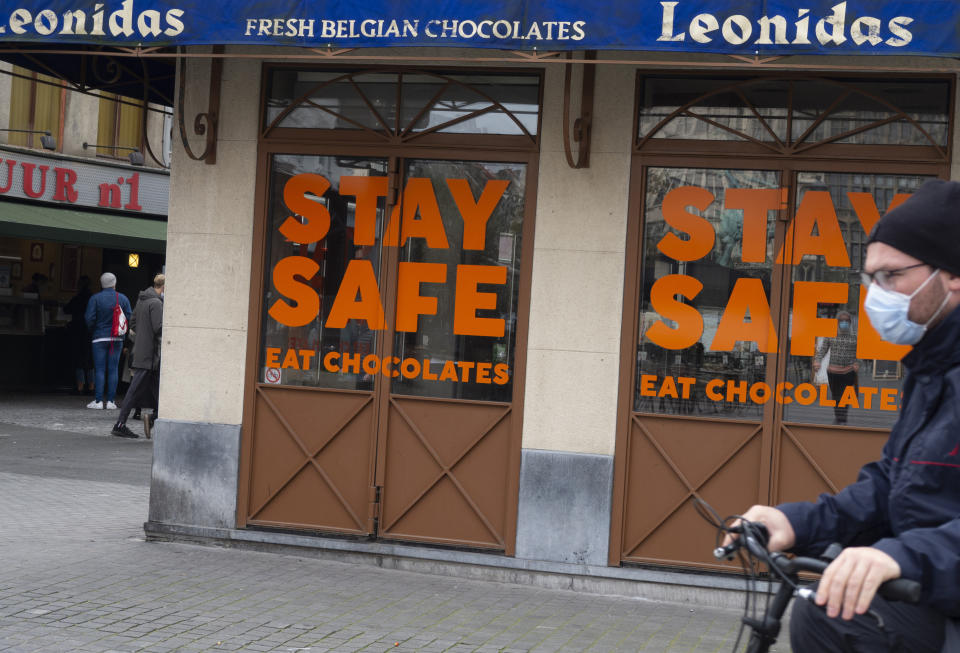 A man cycles by a chocolate shop with a message in the window in the historic center of Antwerp, Belgium, Sunday, Oct. 18, 2020. Faced with a resurgence of coronavirus cases, the Belgian government on Friday announced new restrictions to try to hold the disease in check, including a night-time curfew and the closure of cafes, bars and restaurants for a month. The measures will take effect on Monday, Oct. 19, 2020. (AP Photo/Virginia Mayo)