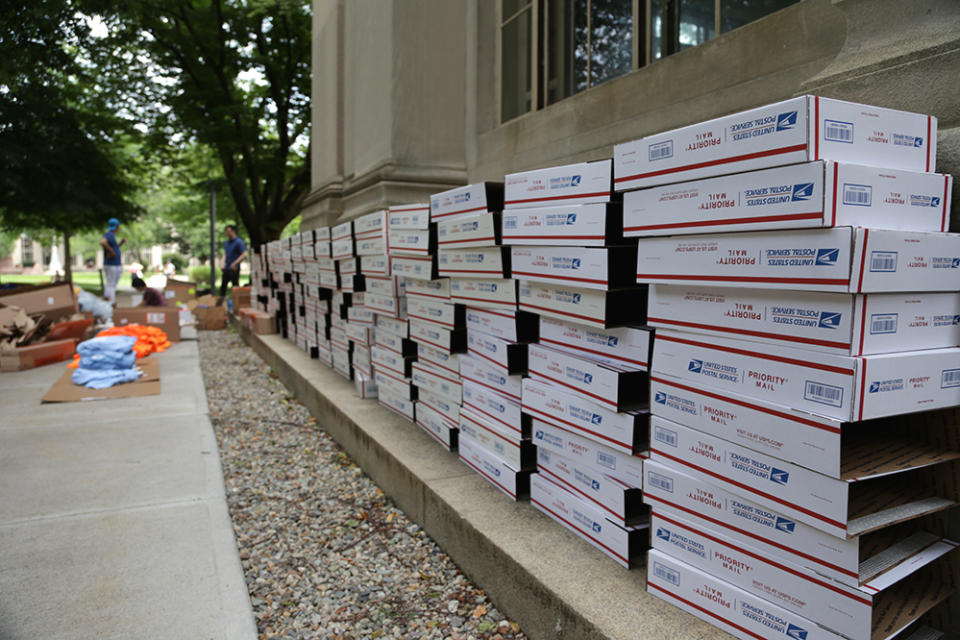 A row of over 100 flat-rate postal shipping boxes line a wall in Killian Court, Cambridge, Massachusetts in preparation for mailing to student mentors (Marianna McMurdock)