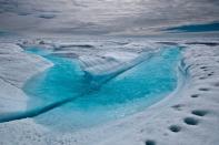 A stream of meltwater flows across the ice surface in Greenland.