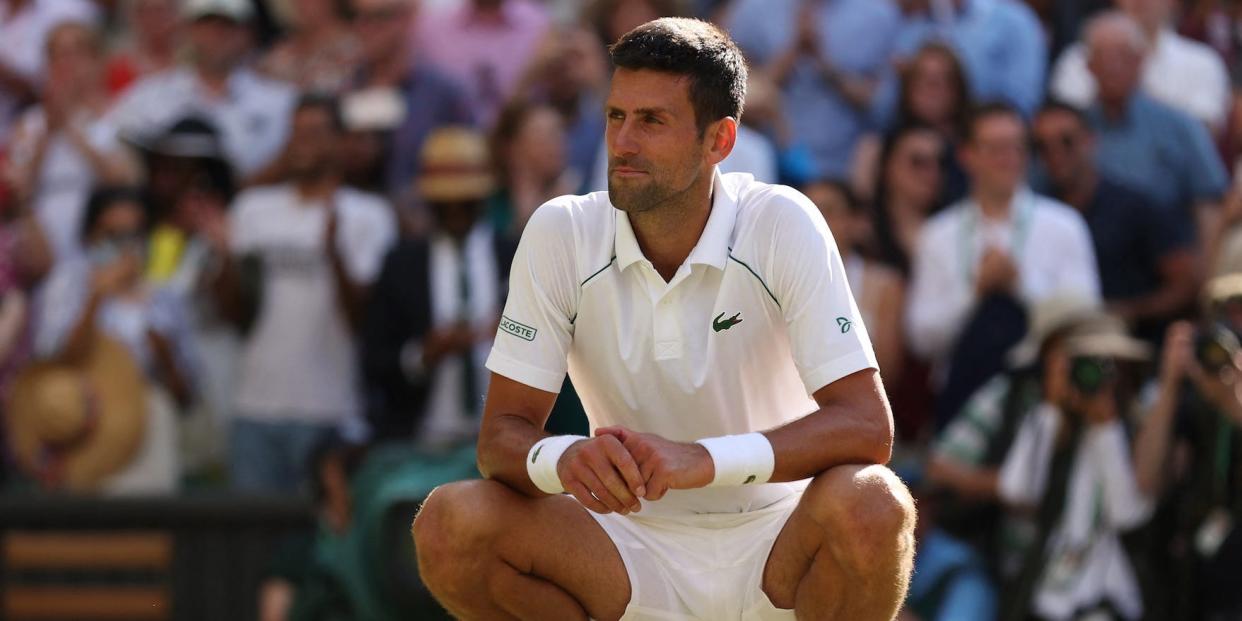 Novak Djokovic squats on the grass after winning Wimbledon.