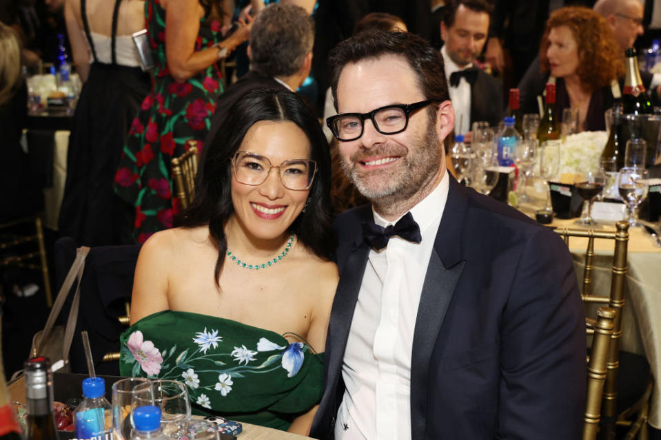 Ali Wong in a floral dress and glasses with a beaded necklace, seated beside a Bill in a tuxedo and bow tie
