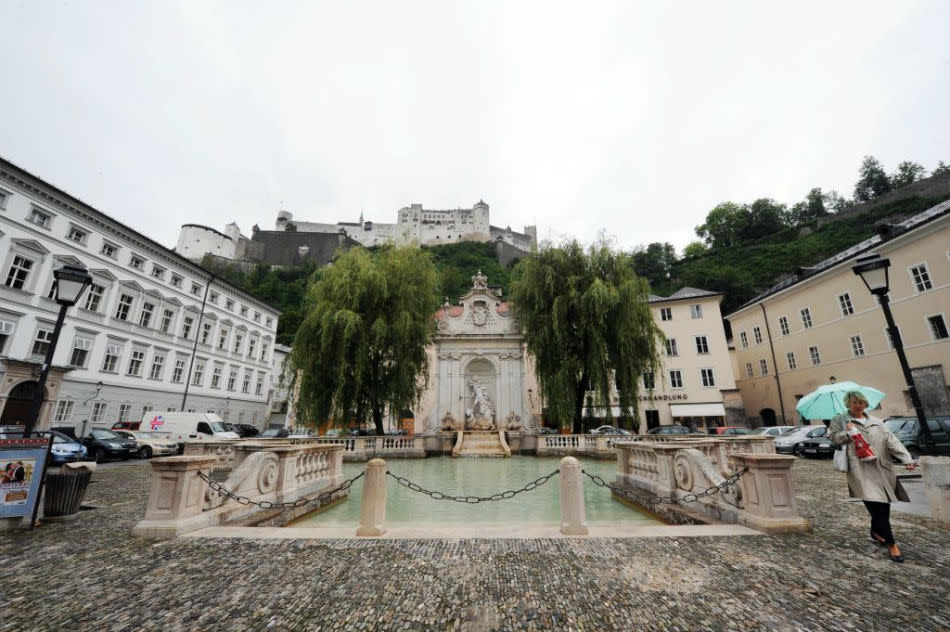 A female tourist with umbrella walks beside the historical horse pond at the Kapitelplatz.