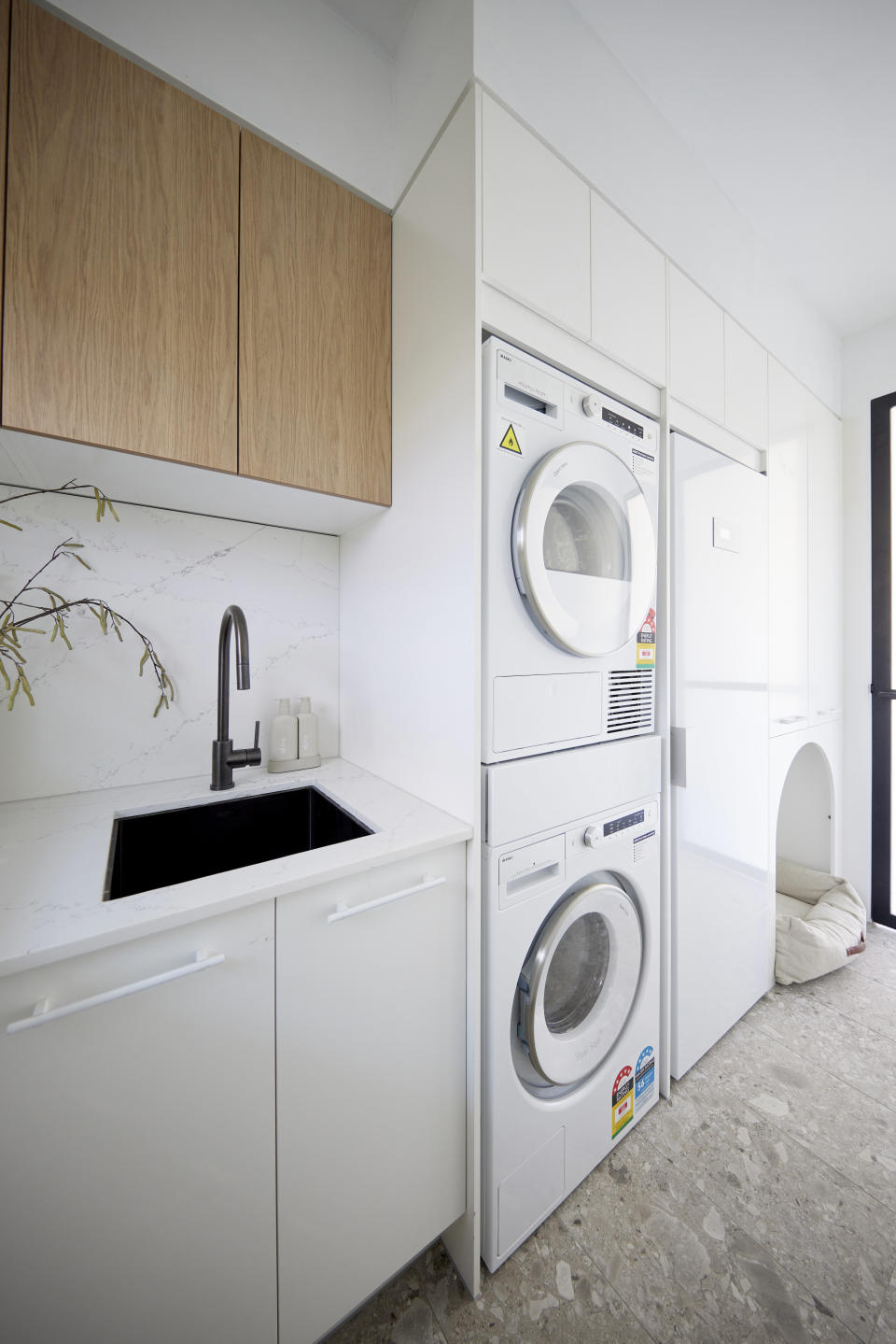 A shot of the laundry with a sink and cupboards on the left and a washer a dryer in the middle stacked on top of each other. 