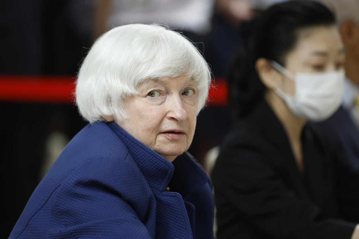 Janet Yellen, wearing a disconcerted expression, with a Japanese woman wearing a surgical mask behind her.