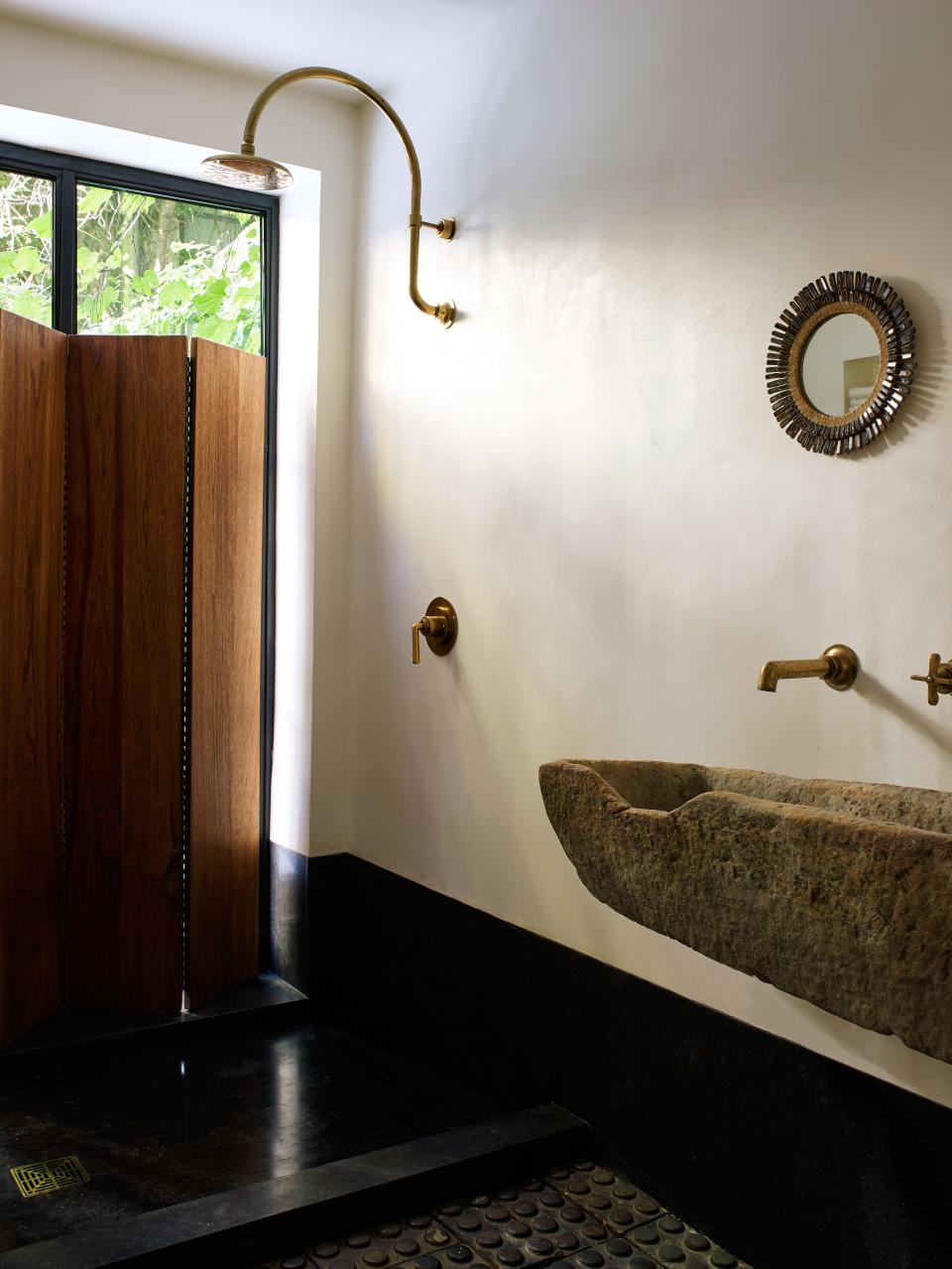 In the downstairs bathroom, Tedhams used one of the antique troughs as a sink, pairing it with an unlacquered brass faucet and showerhead from Waterworks. Above it hangs a mirror by French artist Line Vautrin, a highly collectible piece from the 1950s. The wooden privacy screen was made by Erik Gustafson. “Only an interior designer could live with a bathroom this impractical,” jokes Tedhams.