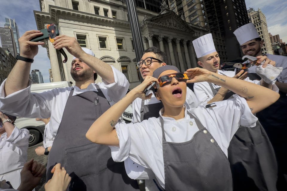 Trabajadores de un restaurant toman un descanso para presenciar el eclipse de Sol, el lunes 8 de abril de 2024, en Nueva York. (AP Foto/John Minchillo)
