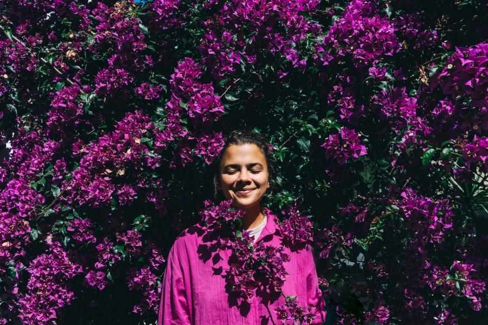 Beautiful, happy woman in a light shirt against the background of a bright purple bougainvillea