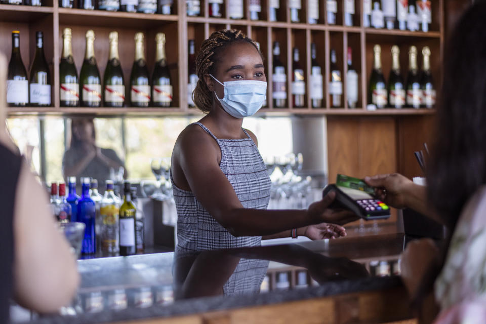 A female bartender wearing a COVID protective face mask serves a customer.