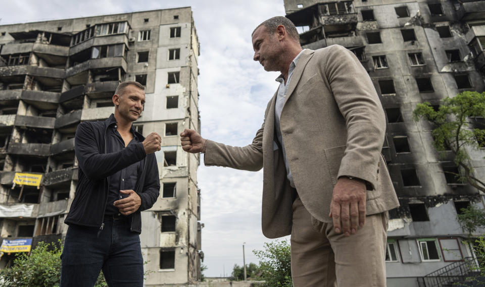 Former striker and coach of the Ukraine national soccer team Andriy Shevchenko, left, exchanges fist bumps with American actor Liev Schreiber in front of a house which have been destroyed by Russia bombardment in Borodianka, near Kyiv, Ukraine, on Monday, Aug. 15, 2022. (AP Photo/Evgeniy Maloletka)