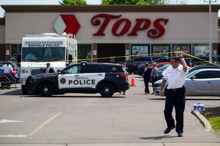 A police officer lifts the tape cordoning off the scene of a shooting at a supermarket, in Buffalo, N.Y., Sunday, May 15, 2022. A white 18-year-old wearing military gear and livestreaming with a helmet camera opened fire with a rifle at a supermarket in Buffalo, killing and wounding people in what authorities described as "racially motivated violent extremism." (AP Photo/Matt Rourke)